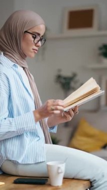 Evdeki oturma odasında kitap okuyan güzel bir genç kadının videosu.