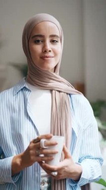 Evdeki oturma odasında ileriye bakarken bir fincan kahve içen genç bir kadının videosu.
