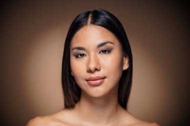 Güzel bir genç kadının, izole edilmiş kahverengi arka planda kameraya poz vermesi.