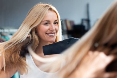 Güzel genç bir kadının banyoda aynaya bakarken saçlarını kurulaması.