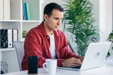 Modern bir girişimde kahve içerken dizüstü bilgisayarla çalışan zeki bir girişimcinin fotoğrafı.