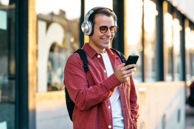 Şehirde kulaklıkla müzik dinlerken akıllı telefon kullanan mutlu bir adamın fotoğrafı.