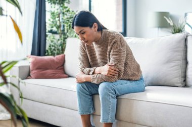 Shot of worried woman thinking about problems sitting on couch in the living room at home clipart