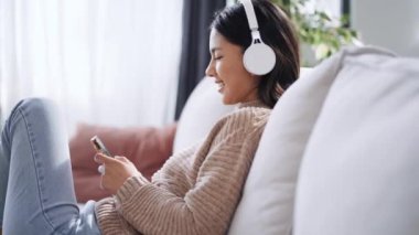 Güzel bir kadının akıllı telefonuyla müzik dinleyip evdeki kanepede dinlendiği bir video..