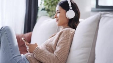 Güzel bir kadının akıllı telefonuyla müzik dinleyip evdeki kanepede dinlendiği bir video..