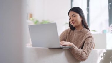 Evdeki kanepede dizüstü bilgisayar kullanan sevimli bir kadının videosu..