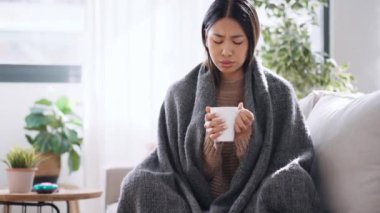 Evdeki kanepede battaniyeyle yatarken çay içen hasta genç kadın videosu.