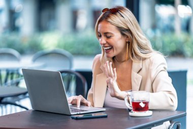 Güzel bir genç bayanın, bilgisayarıyla bir kahve dükkanının terasında akıllı telefon kullanırken görüntüsü..