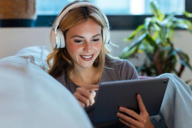 Güzel girişimci kadının dijital tablet kullanırken öğleden sonra koltukta otururken kulaklık kullanması.