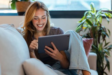 Öğleden sonra koltukta otururken dijital tablet kullanan mutlu girişimci kadın.