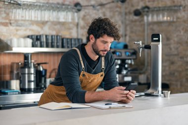 Yakışıklı garsonun, kafeteryada telefonuna kontrol listesi hazırlarken kayıp olan her şeyin envanterini çıkarması.