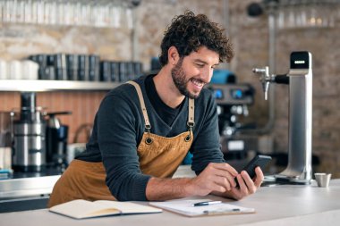 Yakışıklı bir garsonun kahve dükkanında akıllı telefon kullanırken görüntüsü.
