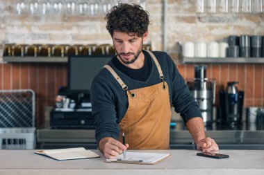 Yakışıklı garsonun, kahve dükkanında kontrol listesi hazırlarken kayıp olan her şeyin envanterini çıkarması.