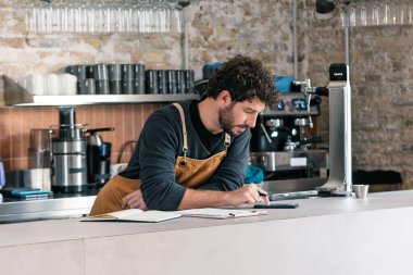 Yakışıklı garsonun, kafeteryada telefonuna kontrol listesi hazırlarken kayıp olan her şeyin envanterini çıkarması.