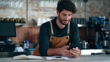 Yakışıklı garsonun kahve dükkanında akıllı telefon kullanırken mola verdiği bir video.