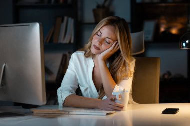 Geceleri ofiste bilgisayarla çalışırken uyuyan güzel bir iş kadınının fotoğrafı..