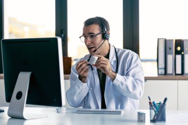 Konsültasyonda, erkek doktorun hastaya tıbbi tedaviyi laptopla ve kulaklıkla yaptığı bir video aramasıyla açıklarken görüntüsü.