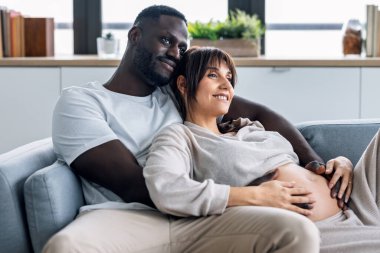 Yakışıklı bir adamın güzel hamile bir kadının karnına dokunurken evdeki kanepede yatarken görüntüsü.