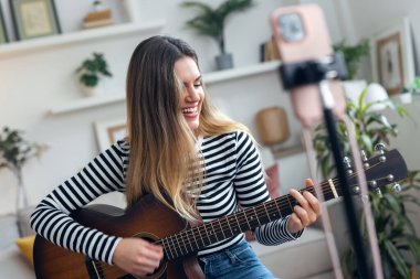 Yemek odasında kendini akıllı telefonuyla kaydederken gitar çalan ve tıngırdatan güzel bir kadın fotoğrafı.