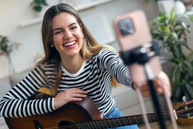 Yemek odasında kendini akıllı telefonuyla kaydederken gitar çalan ve tıngırdatan güzel bir kadın fotoğrafı.