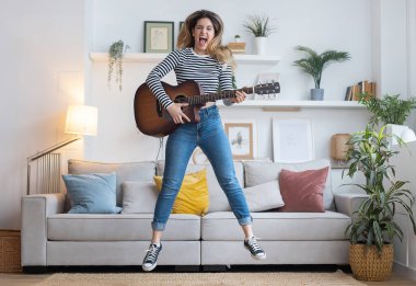Evdeki oturma odasında dans ederken ve zıplarken güzel bir kadının şarkı söyleyip gitar çalması.