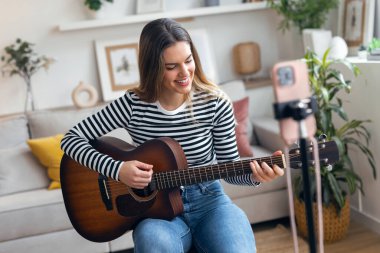 Yemek odasında kendini akıllı telefonuyla kaydederken gitar çalan ve tıngırdatan güzel bir kadın fotoğrafı.