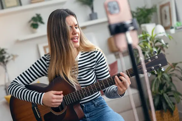 Yemek odasında kendini akıllı telefonuyla kaydederken gitar çalan ve tıngırdatan güzel bir kadın fotoğrafı.