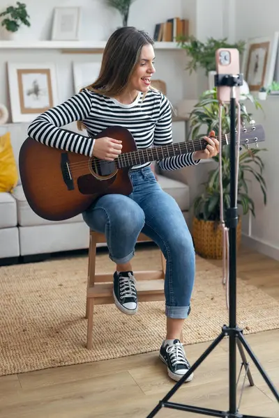 Yemek odasında kendini akıllı telefonuyla kaydederken gitar çalan ve tıngırdatan güzel bir kadın fotoğrafı.