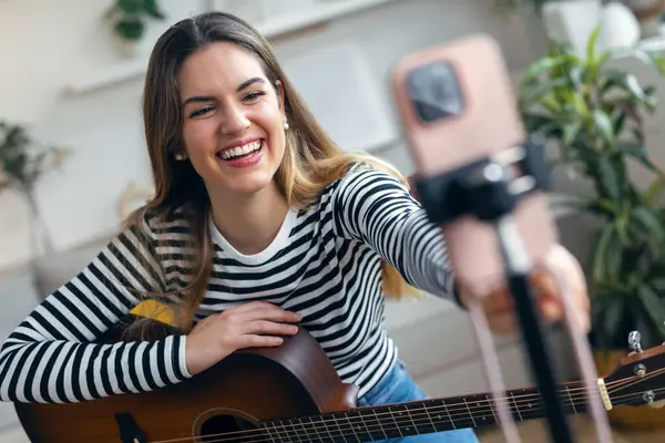 Yemek odasında kendini akıllı telefonuyla kaydederken gitar çalan ve tıngırdatan güzel bir kadın fotoğrafı.