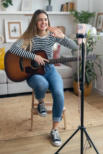 Yemek odasında kendini akıllı telefonuyla kaydederken gitar çalan ve tıngırdatan güzel bir kadın fotoğrafı.