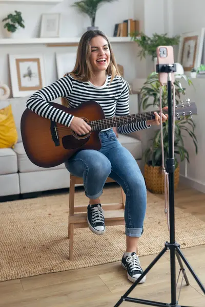 Yemek odasında kendini akıllı telefonuyla kaydederken gitar çalan ve tıngırdatan güzel bir kadın fotoğrafı.