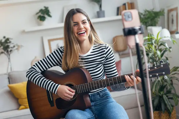 Yemek odasında kendini akıllı telefonuyla kaydederken gitar çalan ve tıngırdatan güzel bir kadın fotoğrafı.