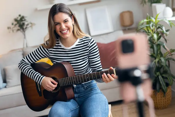 Yemek odasında kendini akıllı telefonuyla kaydederken gitar çalan ve tıngırdatan güzel bir kadın fotoğrafı.