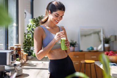 Evdeki mutfakta sebze yeşili el yapımı smoothie içen genç bir kadın..