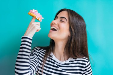 Eğlenceli bir kadının mavi izole edilmiş arka planda pembe çörekle poz vermesi.