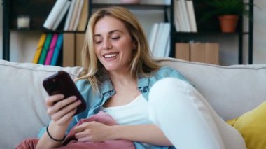 Evdeki koltukta oturan genç ve güzel bir kadının cep telefonunu kullanış videosu.