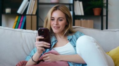 Evdeki koltukta oturan genç ve güzel bir kadının cep telefonunu kullanış videosu.