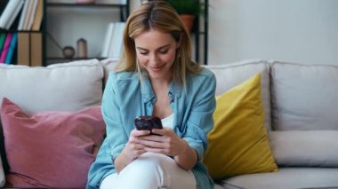 Evdeki koltukta oturan genç ve güzel bir kadının cep telefonunu kullanış videosu.