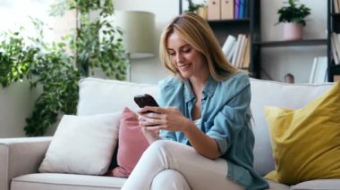 Evdeki koltukta oturan genç ve güzel bir kadının cep telefonunu kullanış videosu.