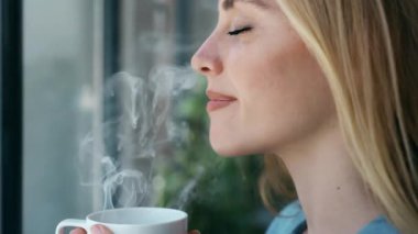 Evdeki oturma odasında kanepede otururken bir fincan kahve içen güzel genç bir kadının videosu..