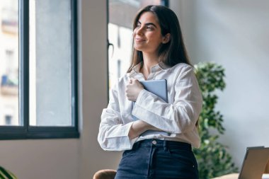 Güzel bir iş kadınının dijital tabletini kullanırken modern bir ofiste ileriye bakarken çekilmiş fotoğrafı.