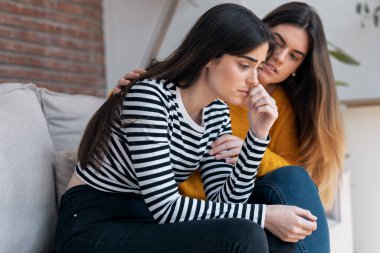 Evdeki kanepede otururken üzgün arkadaşını destekleyen ve rahatlatan güzel bir genç kadın.