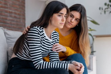 Evdeki kanepede otururken üzgün arkadaşını destekleyen ve rahatlatan güzel bir genç kadın.