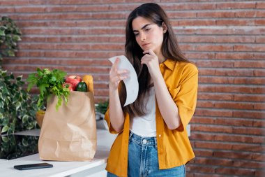 Güzel bir kadının alışveriş biletini kontrol ederken, evde sağlıklı alışverişlerle dolu karton bir çanta bırakması.