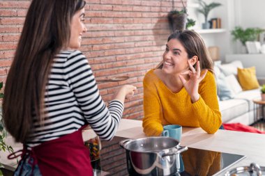 Mutfakta arkadaşına tadına bakarken, güzel bir kadının yemek pişirmesi.