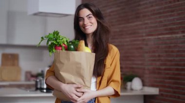 Güzel bir kadının evde akıllı telefon kullanırken elinde sağlık alışverişi torbası olan bir kadın videosu.