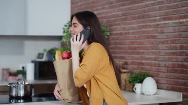 Güzel bir kadının elinde alışveriş poşeti ve evde taze sebzelerle cep telefonuyla konuştuğu bir video.