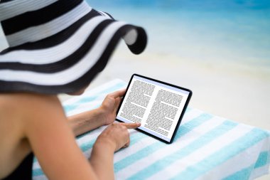 Plajda Tablet Üzerinde E-Kitap Okuyan Kadın