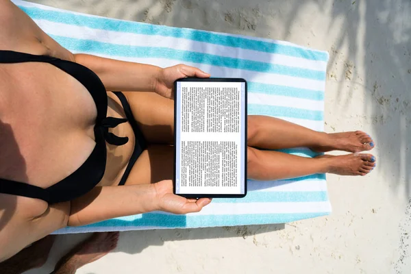 妇女在海滩上阅读电子书 — 图库照片