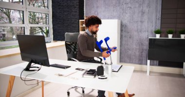 İş yerinde ya da ofiste koltuk değnekleriyle çalışan bir işçi. Rehabilitasyon Yararları